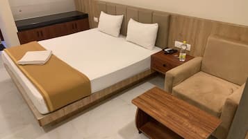 A hotel room with a bed, a bedside table, a chair, and a small wooden table.