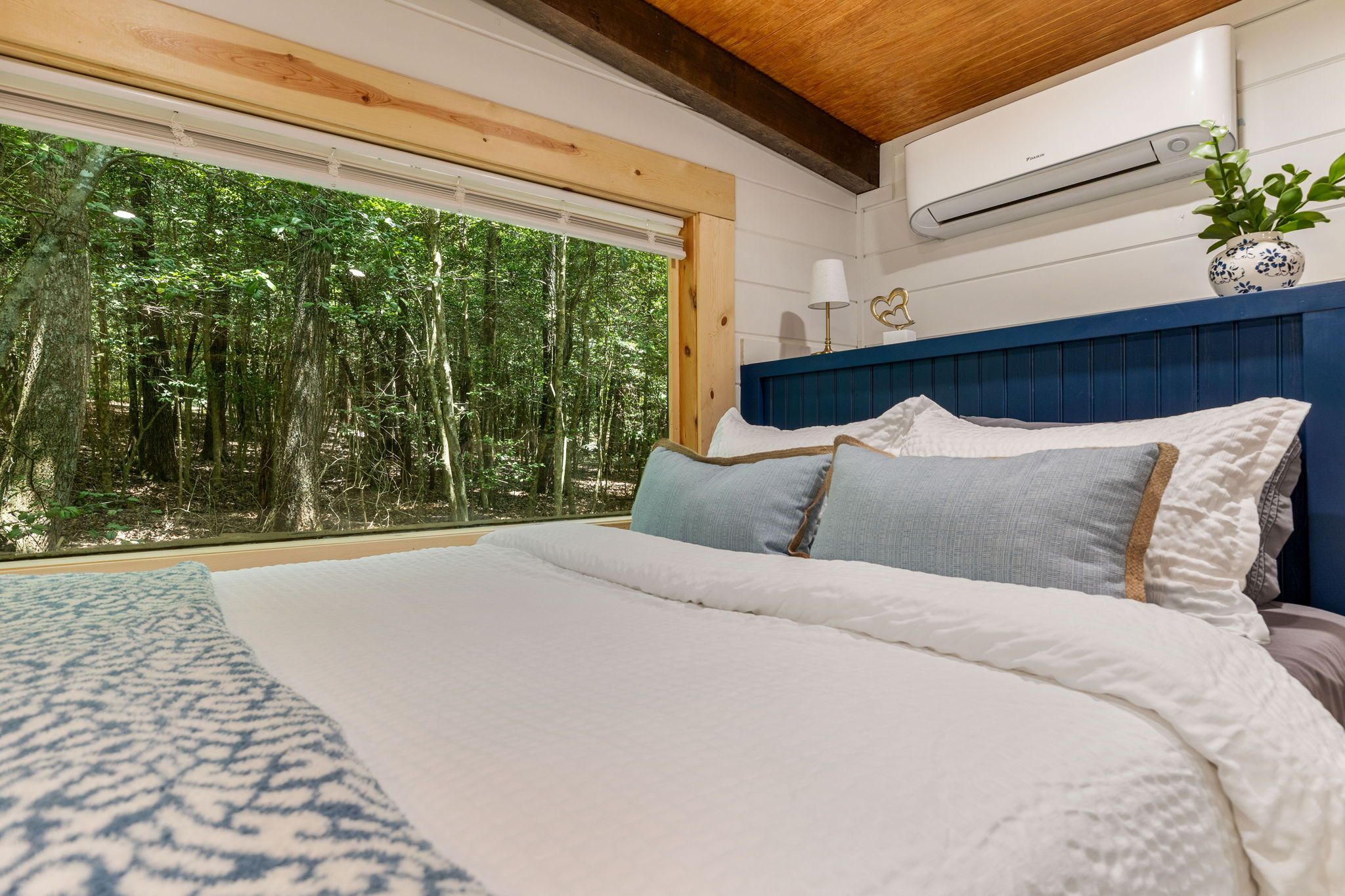 Ein Schlafzimmer mit einem großen Bett, Blick auf einen Wald durch ein Fenster und einer Klimaanlage an der Wand.