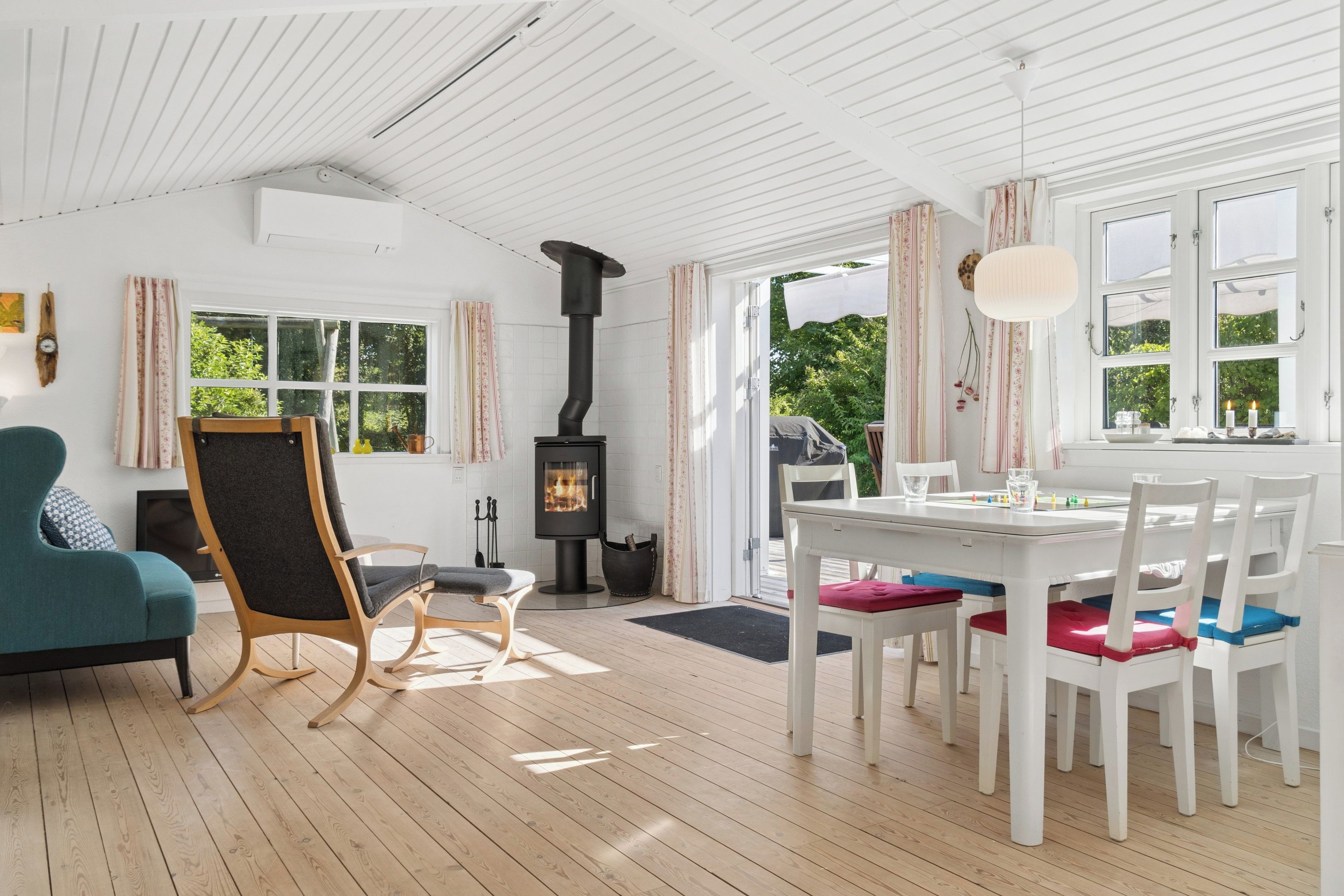 Ein Zimmer mit Holzboden, einem schwarzen Herd, einem Tisch mit Stühlen und einem Fenster mit Vorhängen.