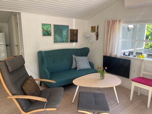A living room with a teal sofa, a round wooden coffee table, a grey armchair, a small white table, and a window with curtains. - Cosy holiday home in beautiful Kulhuse (Jægerspris)