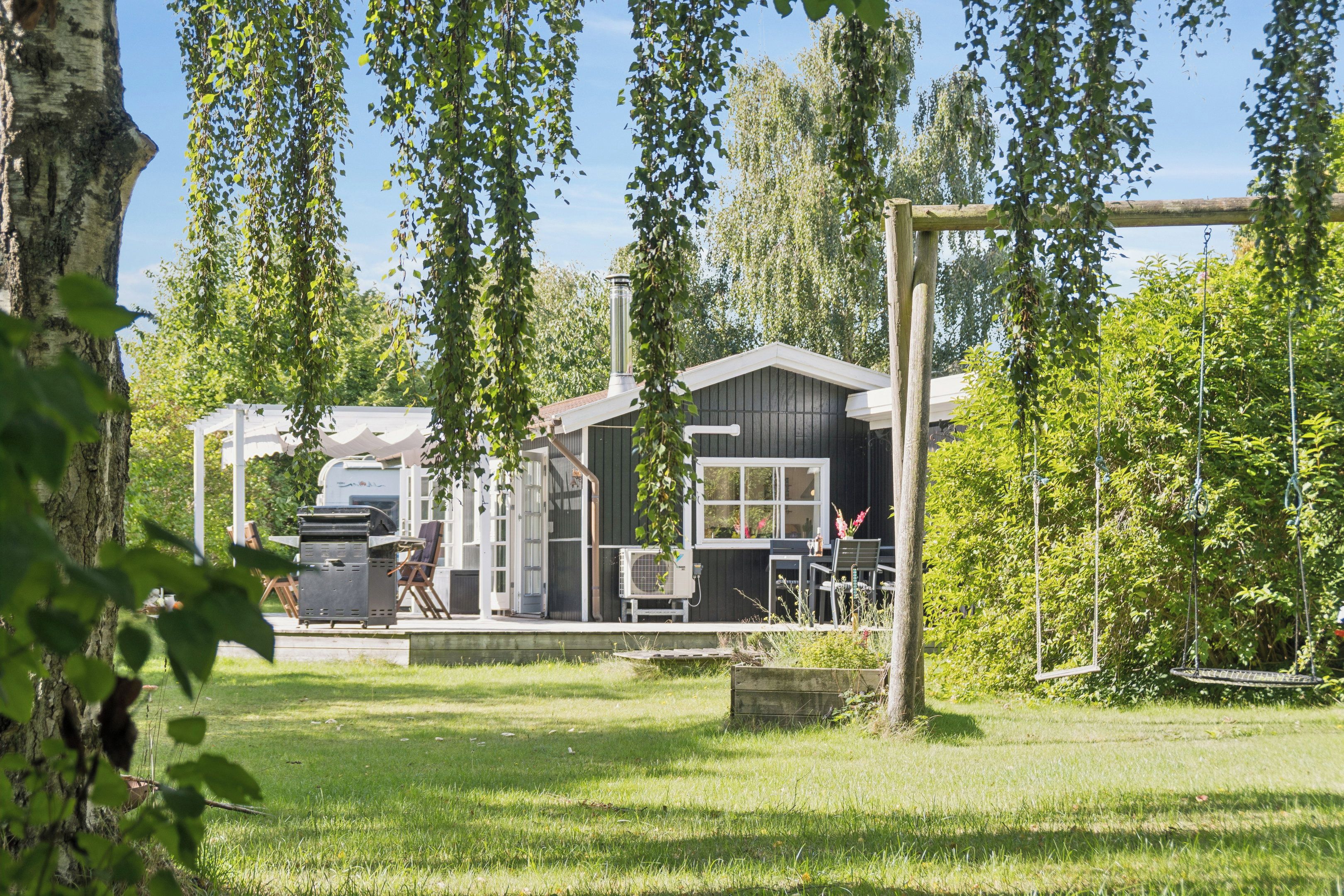 Propiedad residencial con casa, parrilla y un columpio en un patio cubierto de césped.