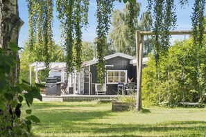 A residential property with a house, a barbecue grill, and a swing set in a grassy yard. - Cosy holiday home in beautiful Kulhuse (Jægerspris)