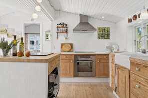 A modern kitchen with wooden cabinets, a built-in oven, and a coffee maker. - Cosy holiday home in beautiful Kulhuse (Jægerspris)