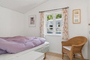 A bedroom with a bed, a chair, a window with curtains, and two framed pictures on the wall. - Cosy holiday home in beautiful Kulhuse (Jægerspris)