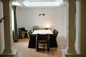 Un coin repas comprenant une table rectangulaire, six chaises, un luminaire suspendu et une fenêtre avec des rideaux.