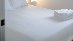 Ein Einzelbett mit weißer Bettwäsche in einem Zimmer mit weißen Wänden und einem Nachttisch.