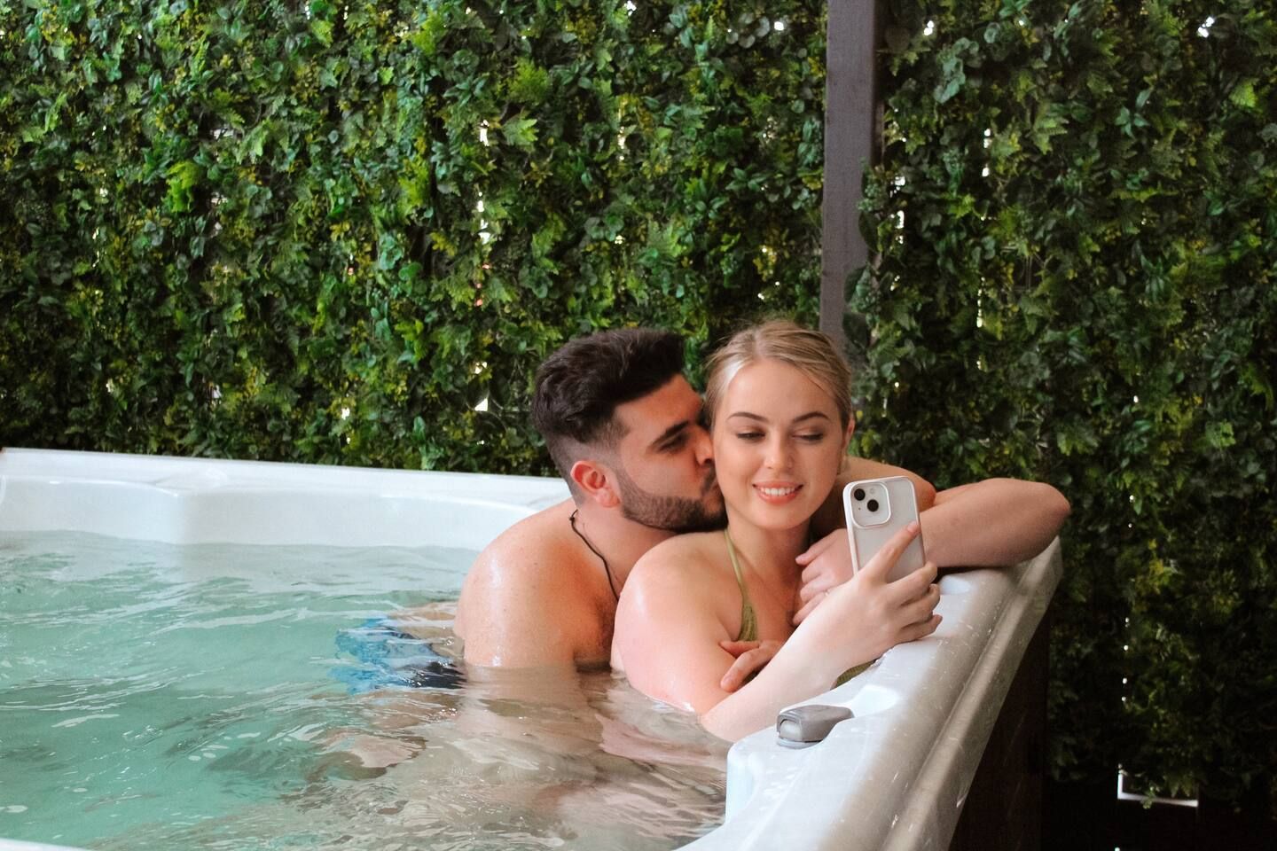 A couple in a hot tub with a lush green wall in the background.