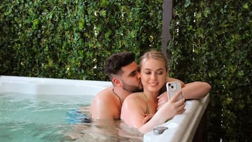 A couple in a hot tub with a lush green wall in the background.