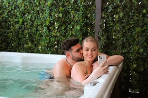 A couple in a hot tub with a lush green wall in the background.