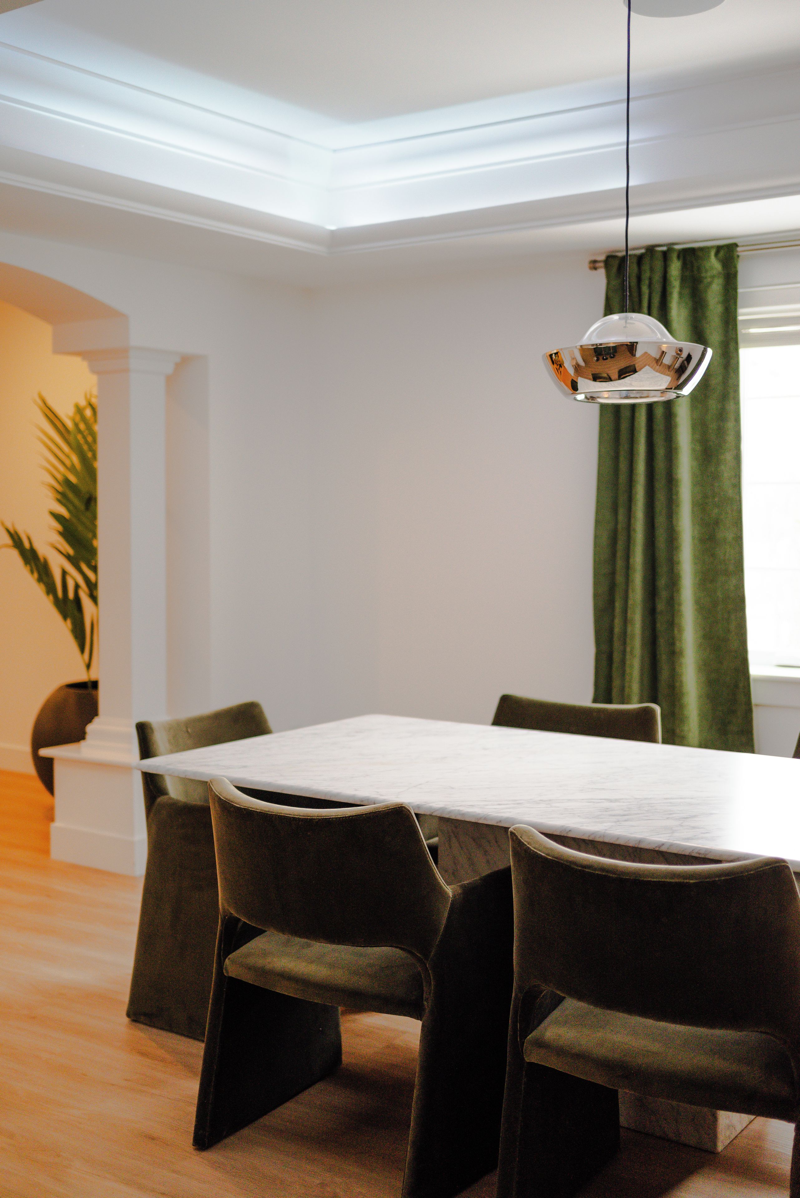 A dining area with a white table and four chairs, a hanging light fixture, and a green curtain.