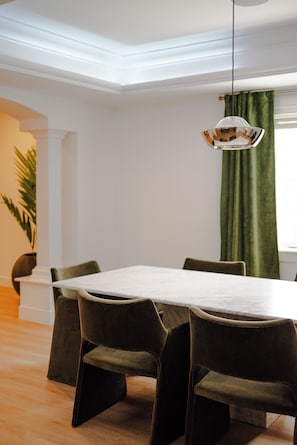 A dining area with a white table and four chairs, a hanging light fixture, and a green curtain.