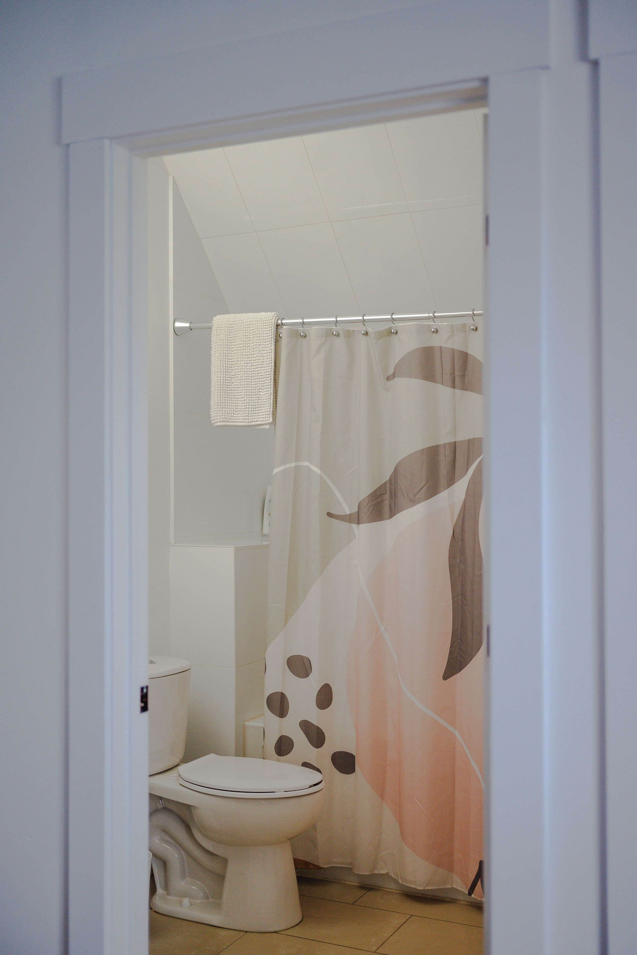 Une salle de bain avec des toilettes, un rideau de douche orné d’un motif de feuilles et une serviette blanche suspendue à une tringle.