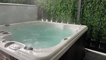 A hot tub with a wooden exterior, surrounded by a wall of green foliage.