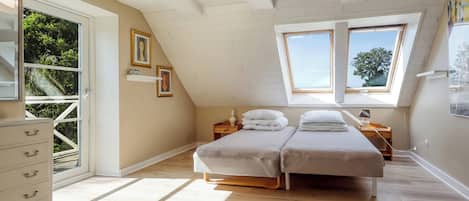 A bedroom with a sloped ceiling, a skylight, a bed, a nightstand, a dresser, and a window.