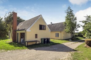 Ein zweistöckiges Haus mit Satteldach, einer Veranda und einem Einfahrt mit Kies.