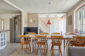 Ein Essbereich mit Holzkästen und einem Tisch, eine Küche mit Kühlschrank und eine Treppe, die zu einer weiteren Ebene führt.