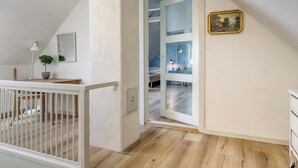 Une pièce avec un plancher en bois, une rambarde blanche, un lit, un bureau, une chaise, une lampe et un tableau accroché au mur.