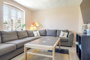 Ein modernes Wohnzimmer mit einem grauen Ecksofa, einem kleinen Couchtisch und einem Fernseher auf einem Schrank.