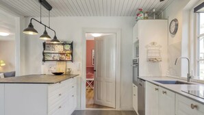 Une cuisine moderne avec des meubles blancs, un four encastré et un évier. On y trouve une étagère avec des livres de cuisine et une horloge au mur.