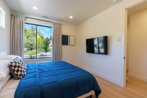 A bedroom with a bed, a window with curtains, a flat-screen TV, and a door. - Designer Townhome Near UO, 3 King Suites + Chefs Kitchen (Eugene)