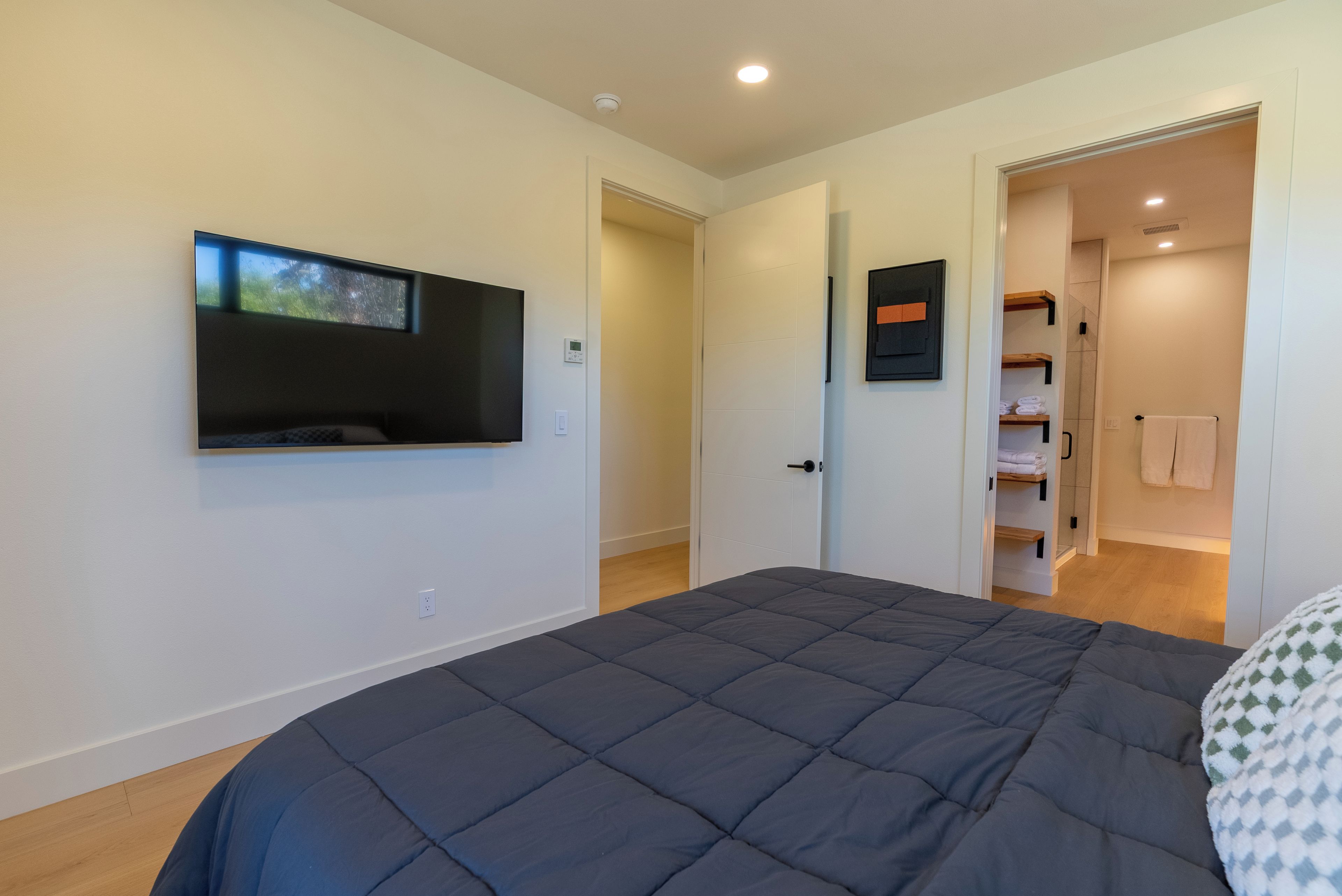 A bedroom with a bed, a television mounted on the wall, and a door leading to a bathroom.