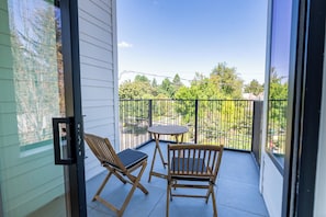 Ein Balkon mit zwei Holzstühlen und einem kleinen Tisch, mit Blick auf eine grüne Landschaft mit Bäumen und einem wolkenlosen Himmel.