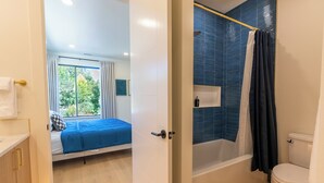 A modern bathroom with a bathtub, toilet, and shower curtain. - Designer Townhome Near UO, 3 King Suites + Chefs Kitchen (Eugene)