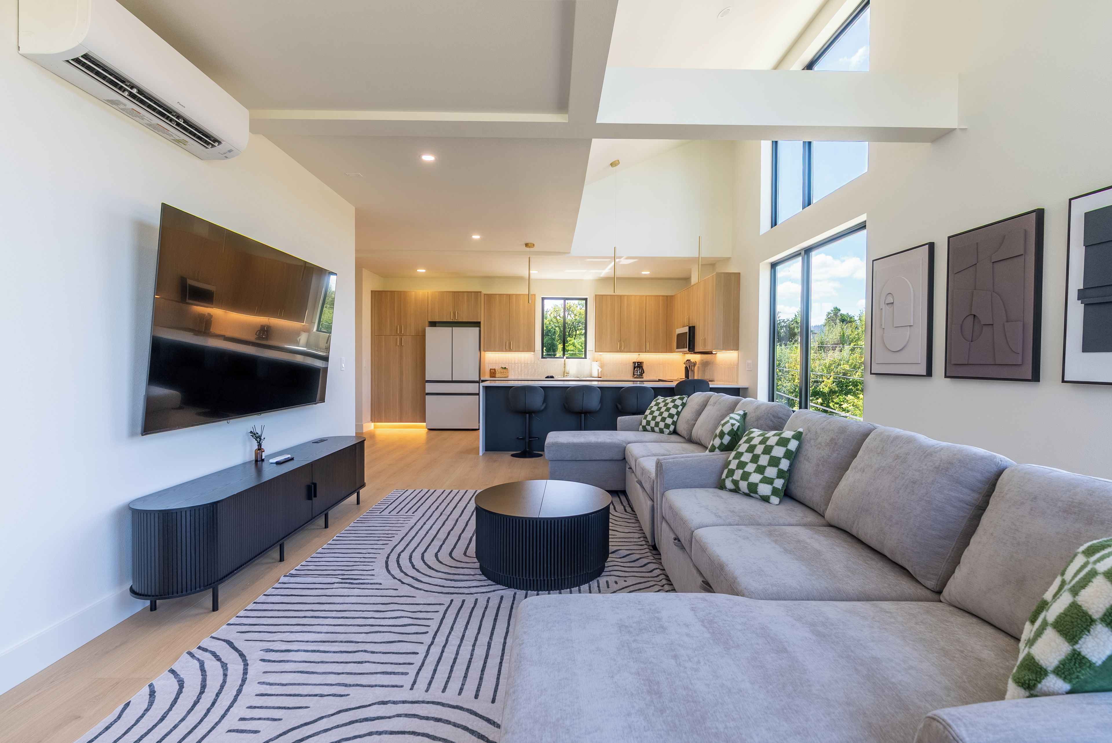 A modern living room with a large flat-screen TV, a sectional sofa, and a patterned rug.