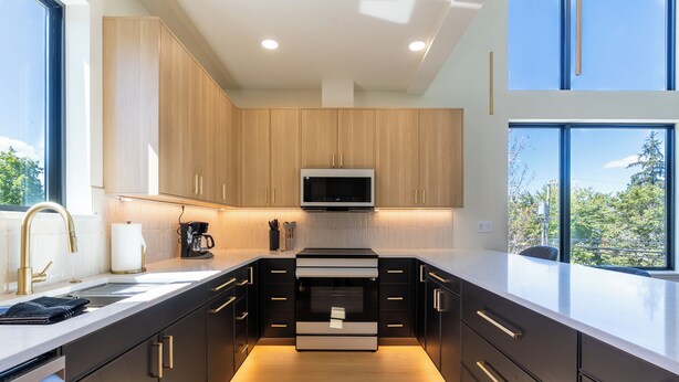 A modern kitchen with a central island, built-in appliances, and a large window providing a view of the outdoors. - Designer Townhome Near UO, 3 King Suites + Chefs Kitchen (Eugene)