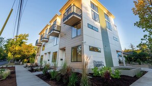 A multi-story residential building with balconies, large windows, and a landscaped garden area. - Designer Townhome Near UO, 3 King Suites + Chefs Kitchen (Eugene)