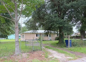 A single-story house with a front yard, a fenced area, and a blue trash bin.
