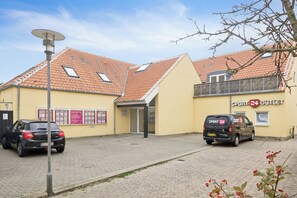 Ein Gebäude mit einer gelben Fassade, einem roten Ziegeldach und einem Schild für 'Sport 24 Outlet'. Vor dem Gebäude sind zwei Autos geparkt.
