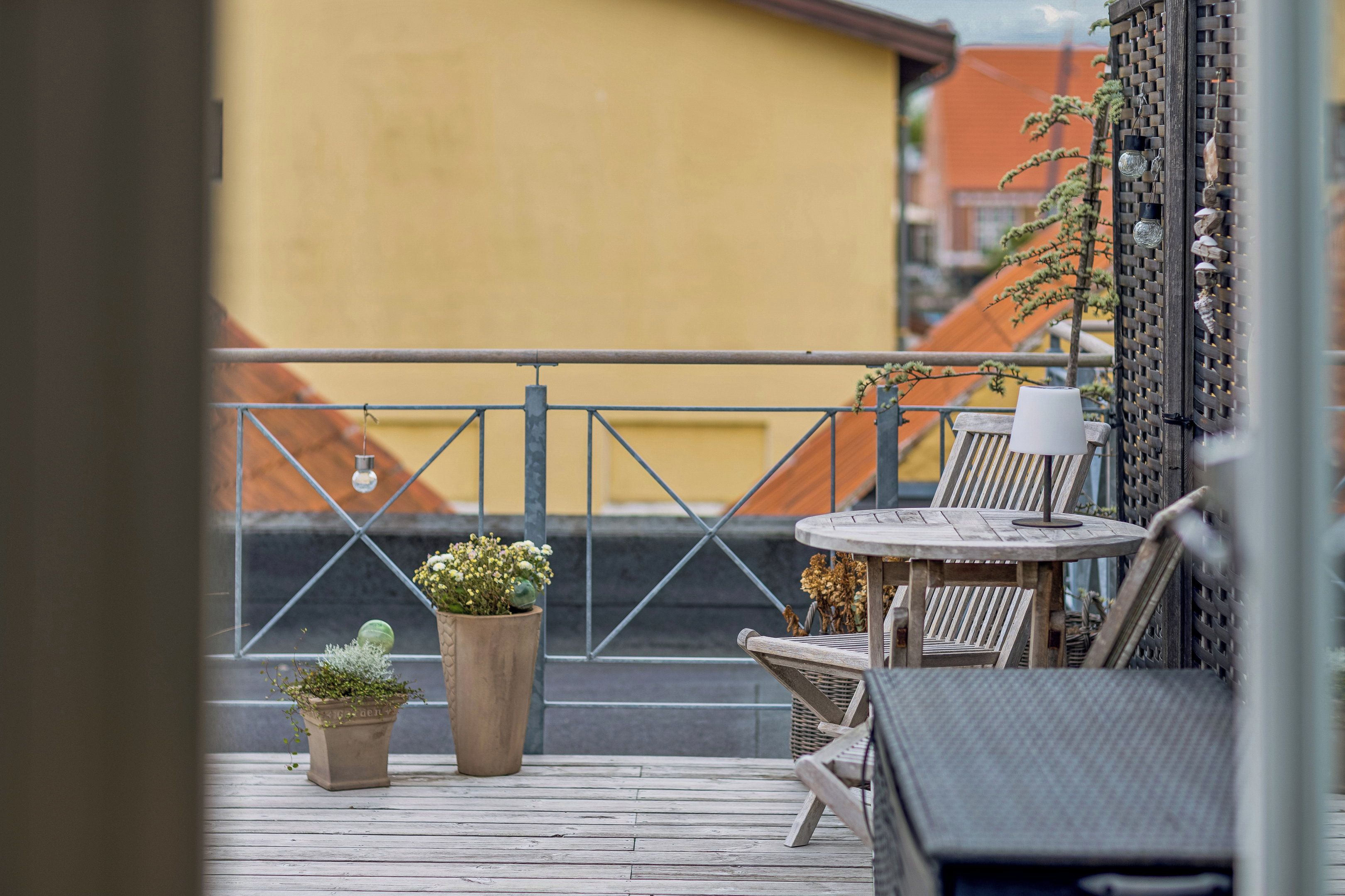 Une terrasse en bois avec deux plantes en pot, une table ronde et une chaise.