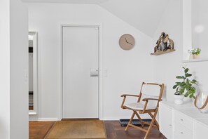 A room with a white door, a wooden chair, a clock, a shelf with decorative items, and a potted plant. - Lovely apartment in the heart of Skagen town (Skagen)