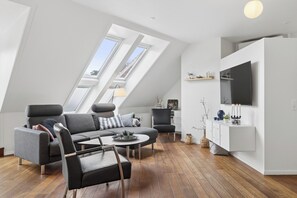 Ein modernes Loft-Apartment mit schrägem Dach, einem Ecksofa, einem Esstisch und einem an der Wand befestigten Flachbildfernseher.