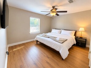 A bedroom with a bed, a ceiling fan, a nightstand with a lamp, and a window with blinds.