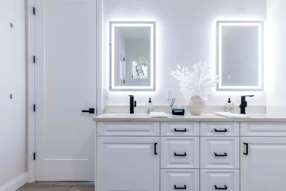A bathroom with two large mirrors, a white vanity with drawers, and a small vase with white flowers.