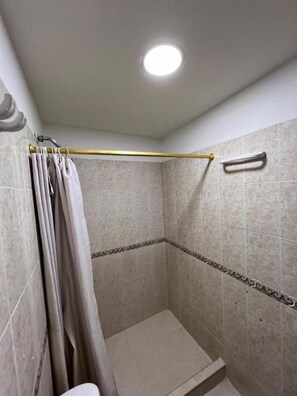 Un espacio de ducha pequeño y cerrado, con cortina, toallero y un escalón para acceder a la ducha.