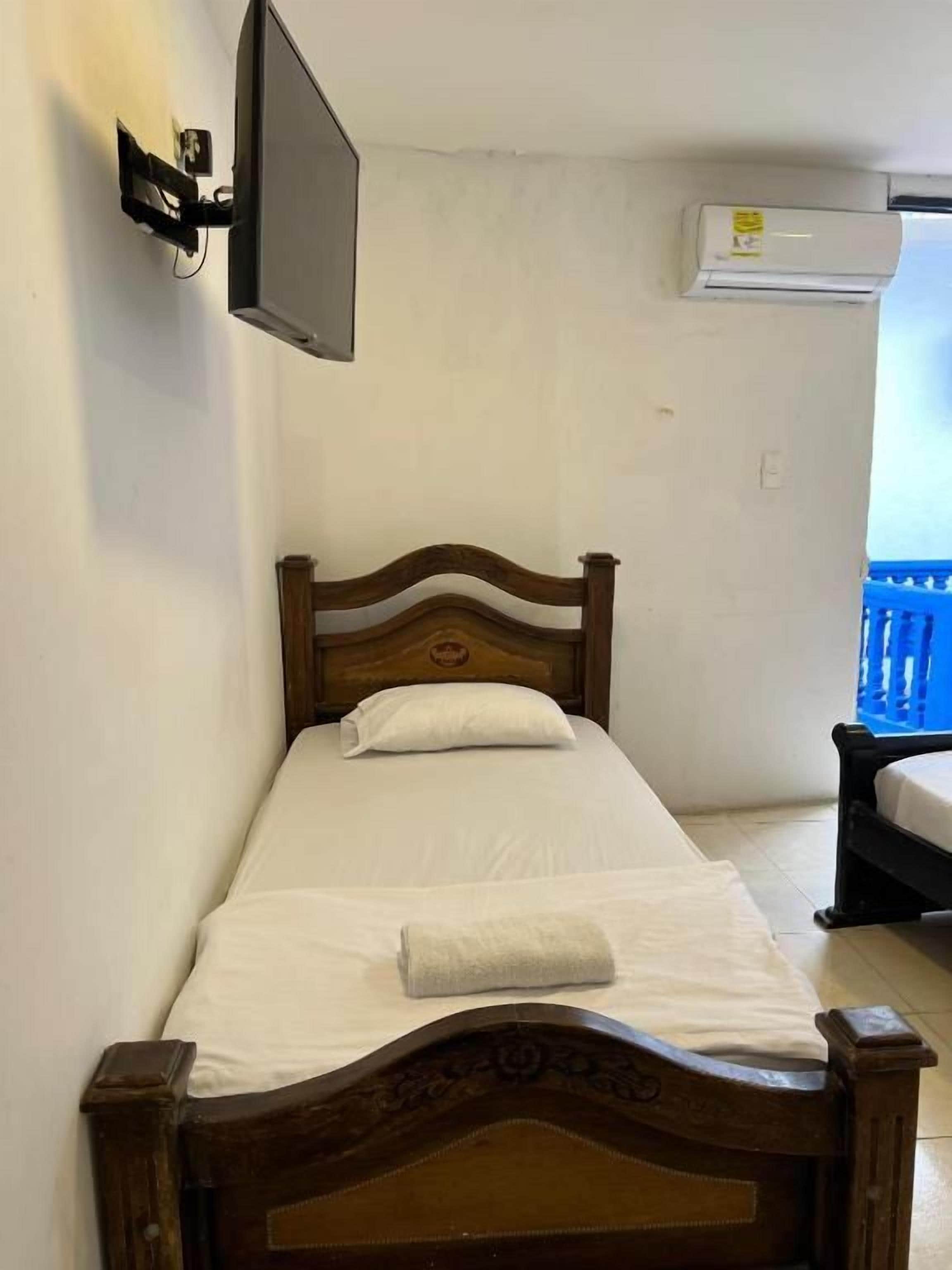 Una cama individual con cabecera de madera, un televisor de pantalla plana montado en la pared y un equipo de aire acondicionado.