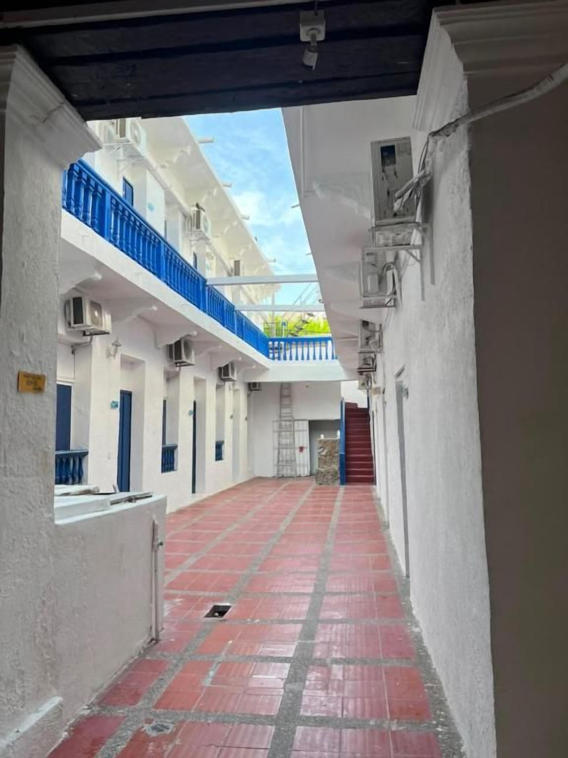Un pasillo con piso de baldosas rojas, paredes blancas y barandillas azules en balcones.