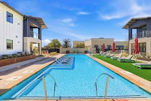 Una piscina con sillones reclinables y sombrillas, rodeada de edificios modernos.