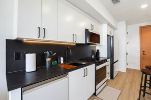 Una cocina moderna con armarios blancos, encimera negra y electrodomésticos de acero inoxidable.