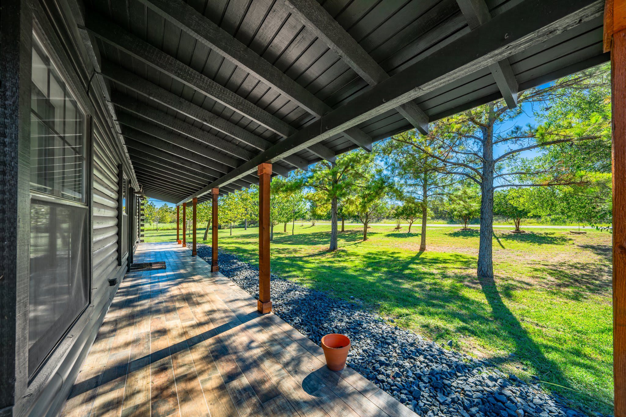 A covered porch with a view of a grassy park and trees.