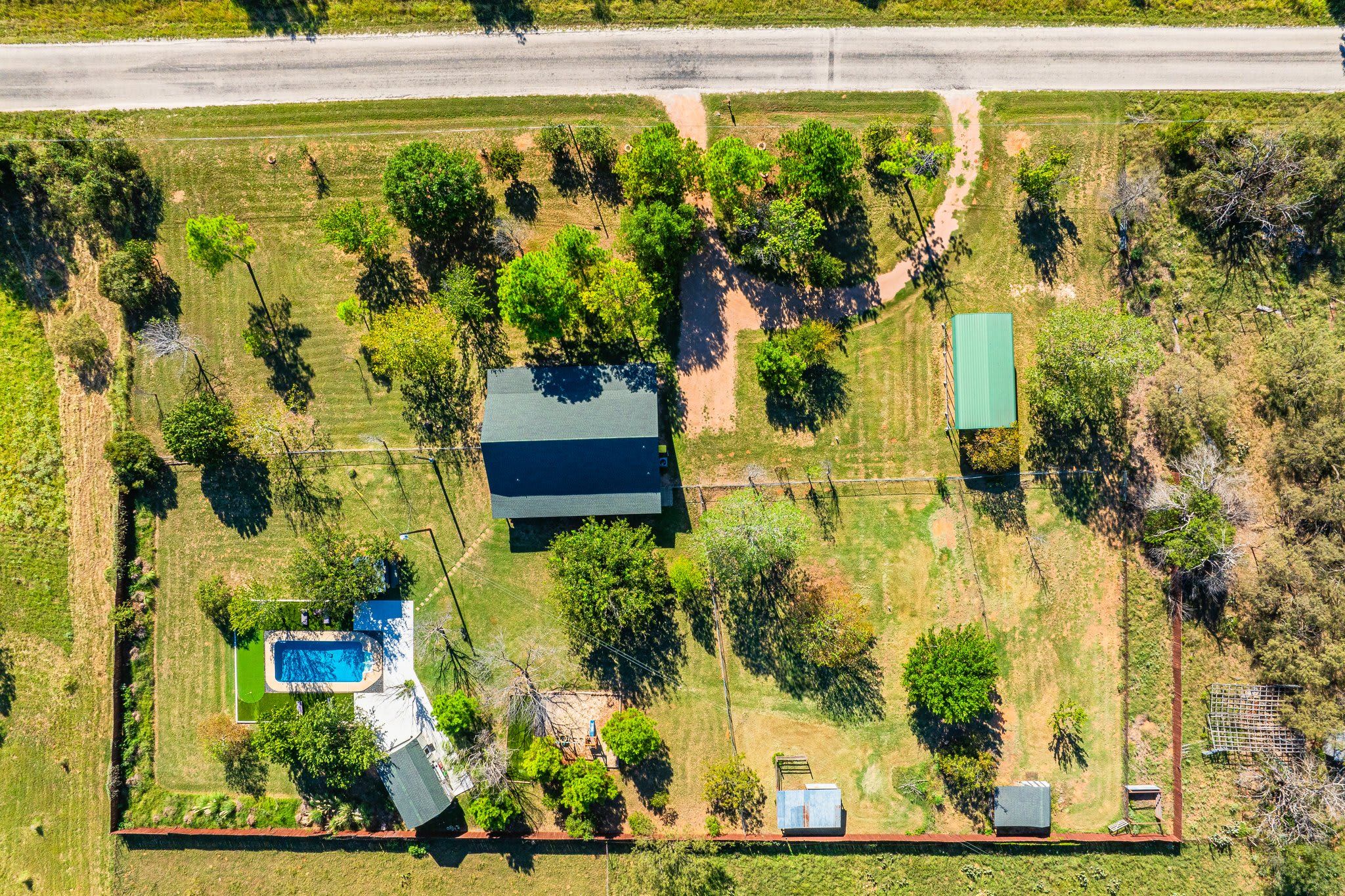 An aerial view of a property with a swimming pool, a fenced yard, and a building with a green roof.