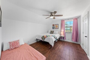A bedroom with a bed, a smaller bed, a ceiling fan, a window with curtains, and a door. - Casa Boots & Bubbly w/ Pool, Sleeps 14 (Fredericksburg)