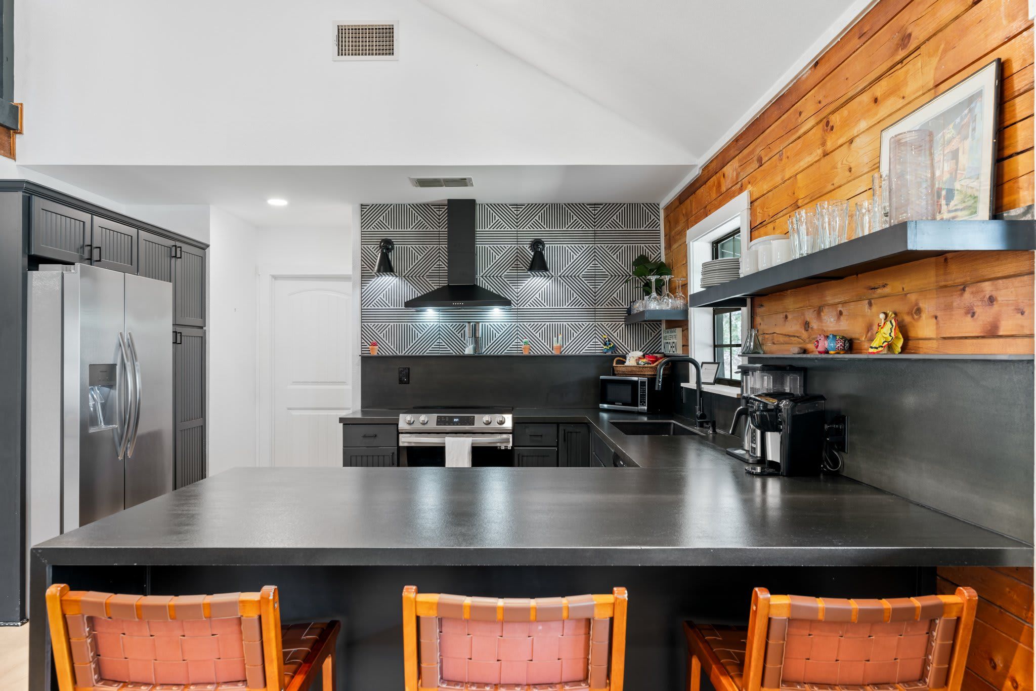 A modern kitchen with a large island, stainless steel appliances, and a geometric backsplash.