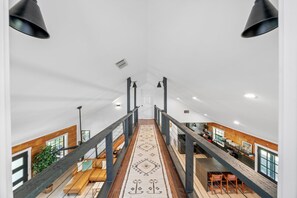 A spacious interior with a central staircase, wooden beams, and a view of a kitchen area. - Casa Boots & Bubbly w/ Pool, Sleeps 14 (Fredericksburg)