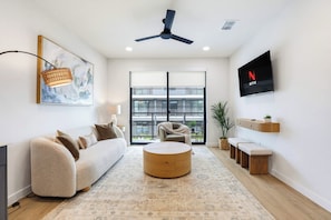 A modern living room with a sofa, round coffee table, and a flat-screen TV mounted on the wall. - Luxury Condo With Pool-view Balcony (New Braunfels)