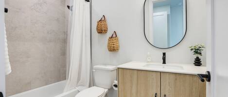 A bathroom with a shower, toilet, vanity, and a mirror.