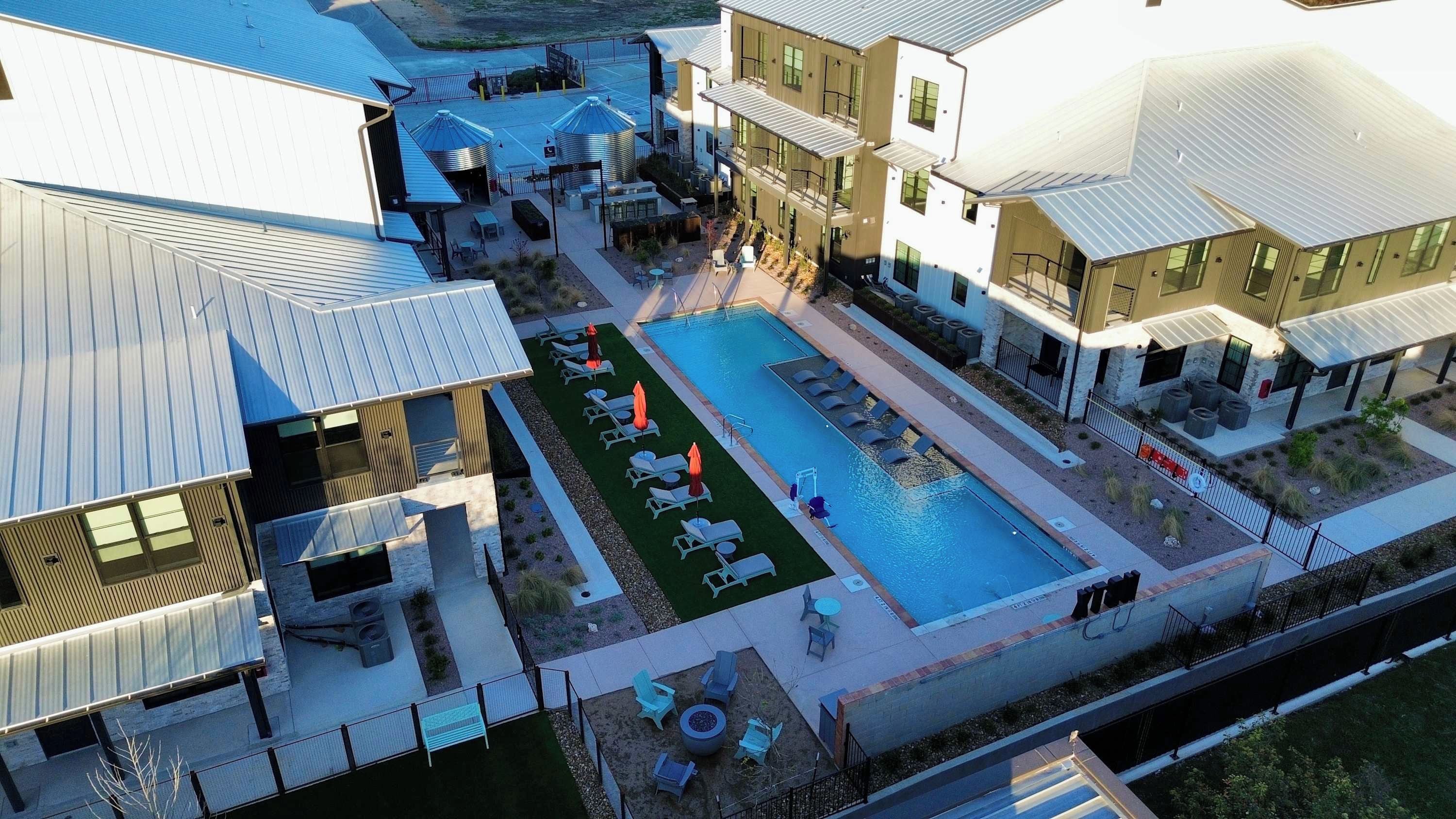 Un edificio moderno con piscina, mobiliario exterior y un patio cercado.
